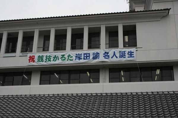 市役所の壁に「祝 競技かるた 岸田 諭 名人誕生」の垂れ幕が掛かっている写真